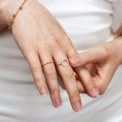 Close-up of a hand wearing a 9ct solid gold open circle diamond ring with a pavé-set diamond halo, styled alongside a delicate diamond band and a gold bead bracelet.