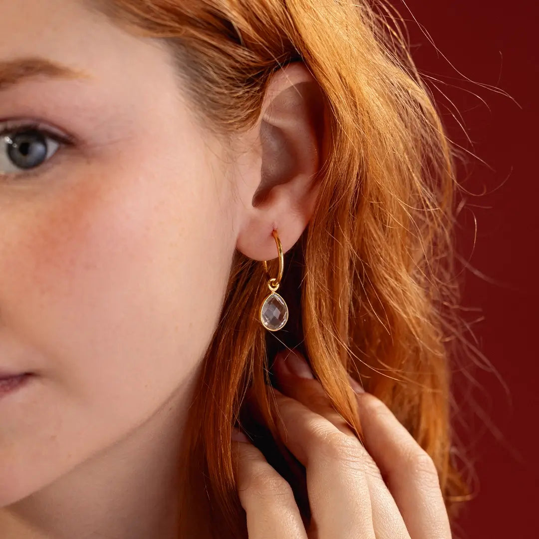 Model wearing gold hoop earring with faceted white quartz gemstone drop