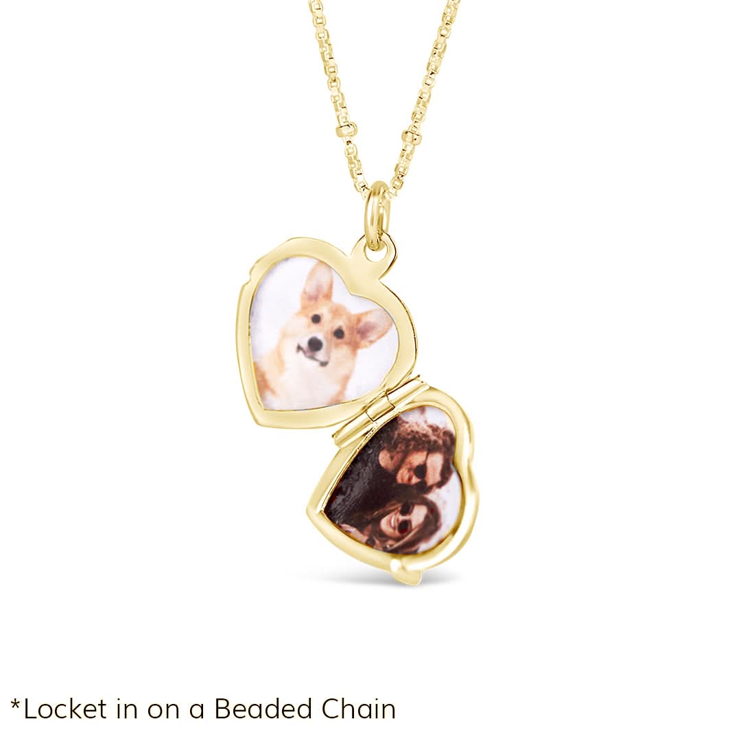 Product image showing a gold heart-shaped locket necklace opened to reveal two custom photos inside – one of a dog and one of a couple. The locket features a diamond star engraving on the front and hangs on a fine beaded chain. Shown against a clean white background