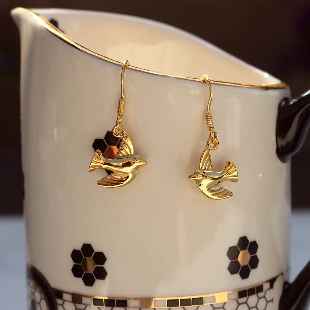 Gold vermeil bird drop earrings hanging on a ceramic jug, featuring delicate flying bird charms with polished finish.