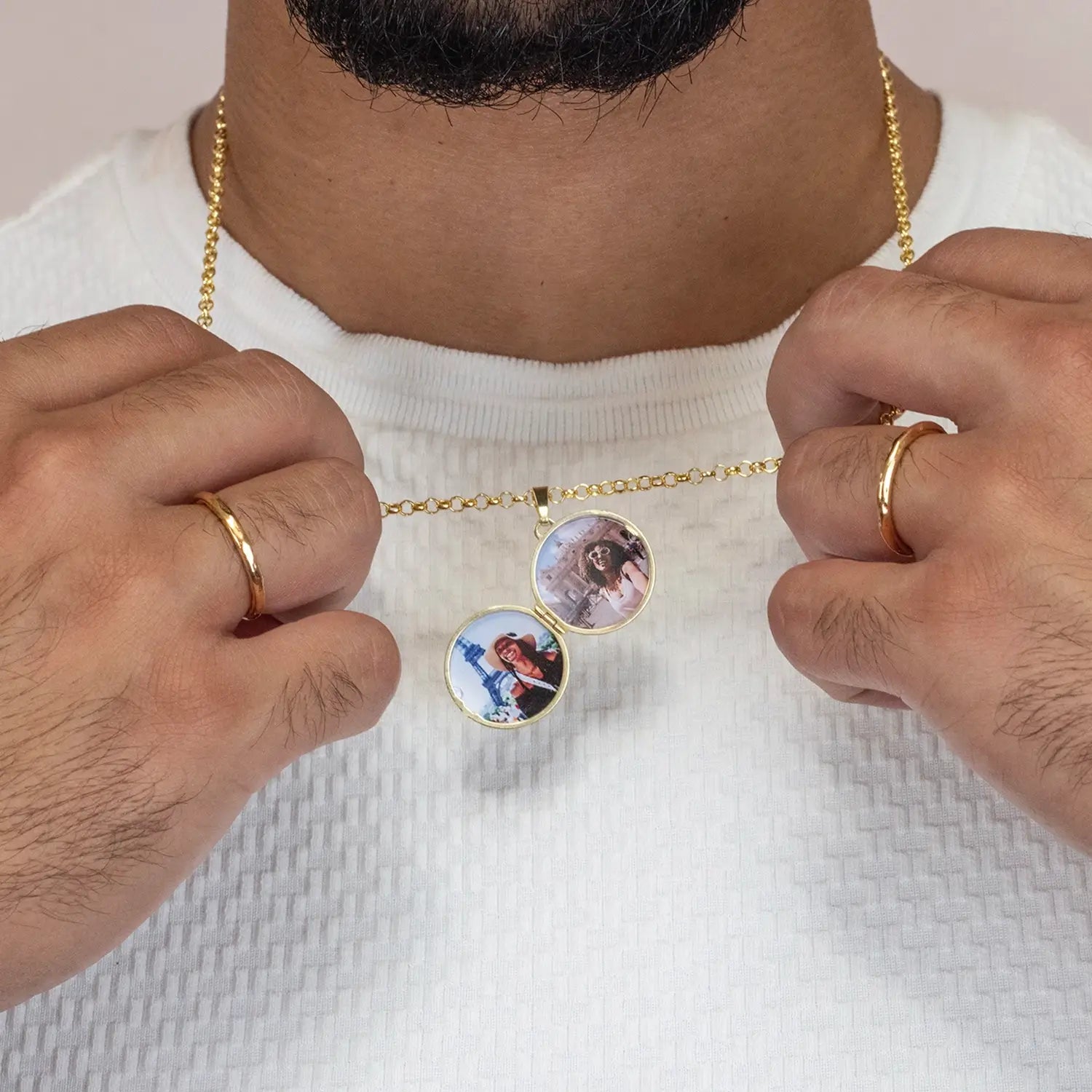 man wearing a gold compass necklace with two round photos, wearing a white shirt