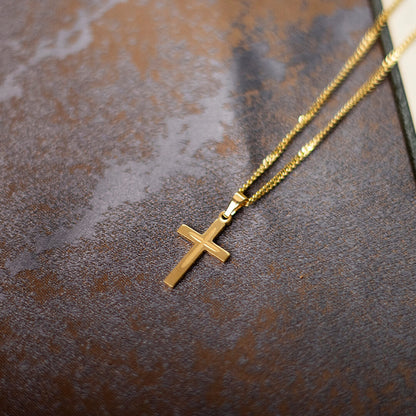 small gold cross necklace on chain, lying on textured leather