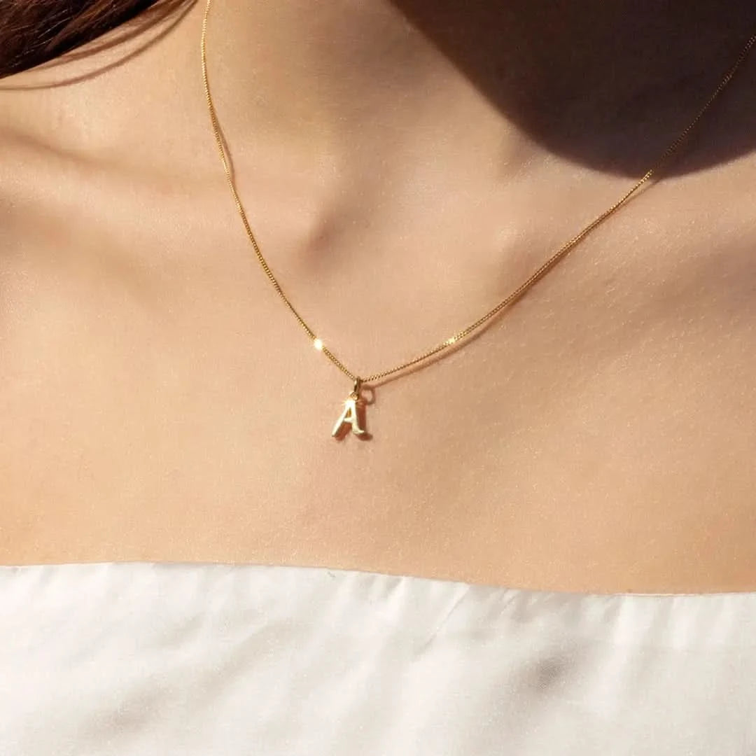 Close-up of a female model wearing a strapless white silk top and the 9-carat solid gold initial necklace, letter 'A', on a close curb chain. 