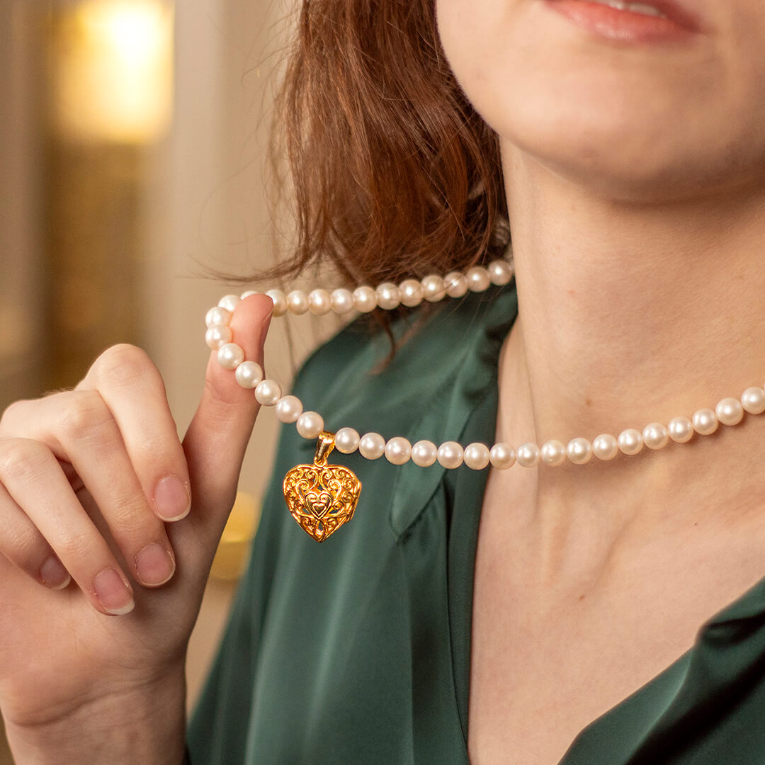 Model wearing white pearl necklace with gold filigree heart locket 