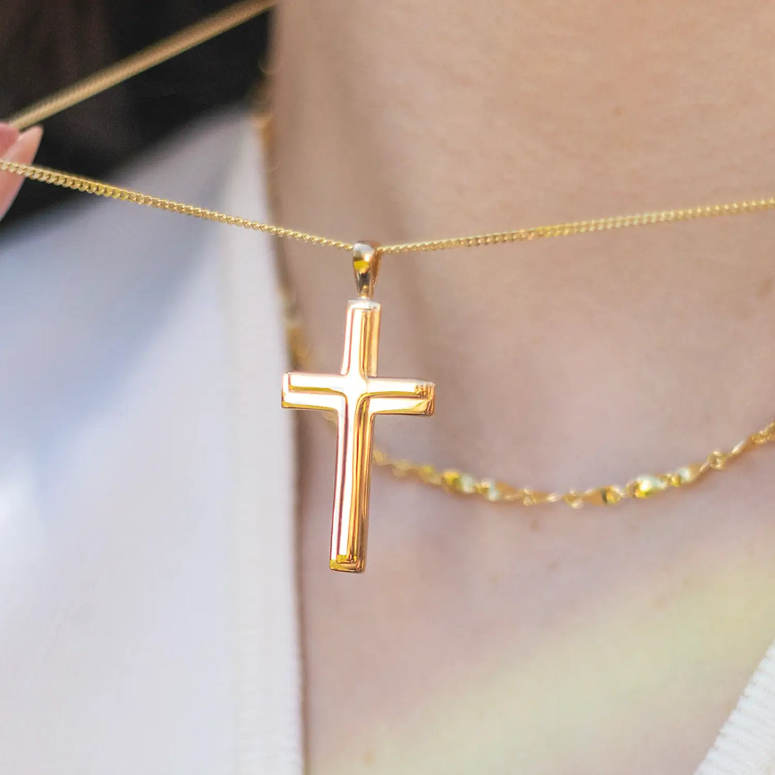 close up shot of a woman wearing a gold heavy cross necklace and holding the chain out with her hand 