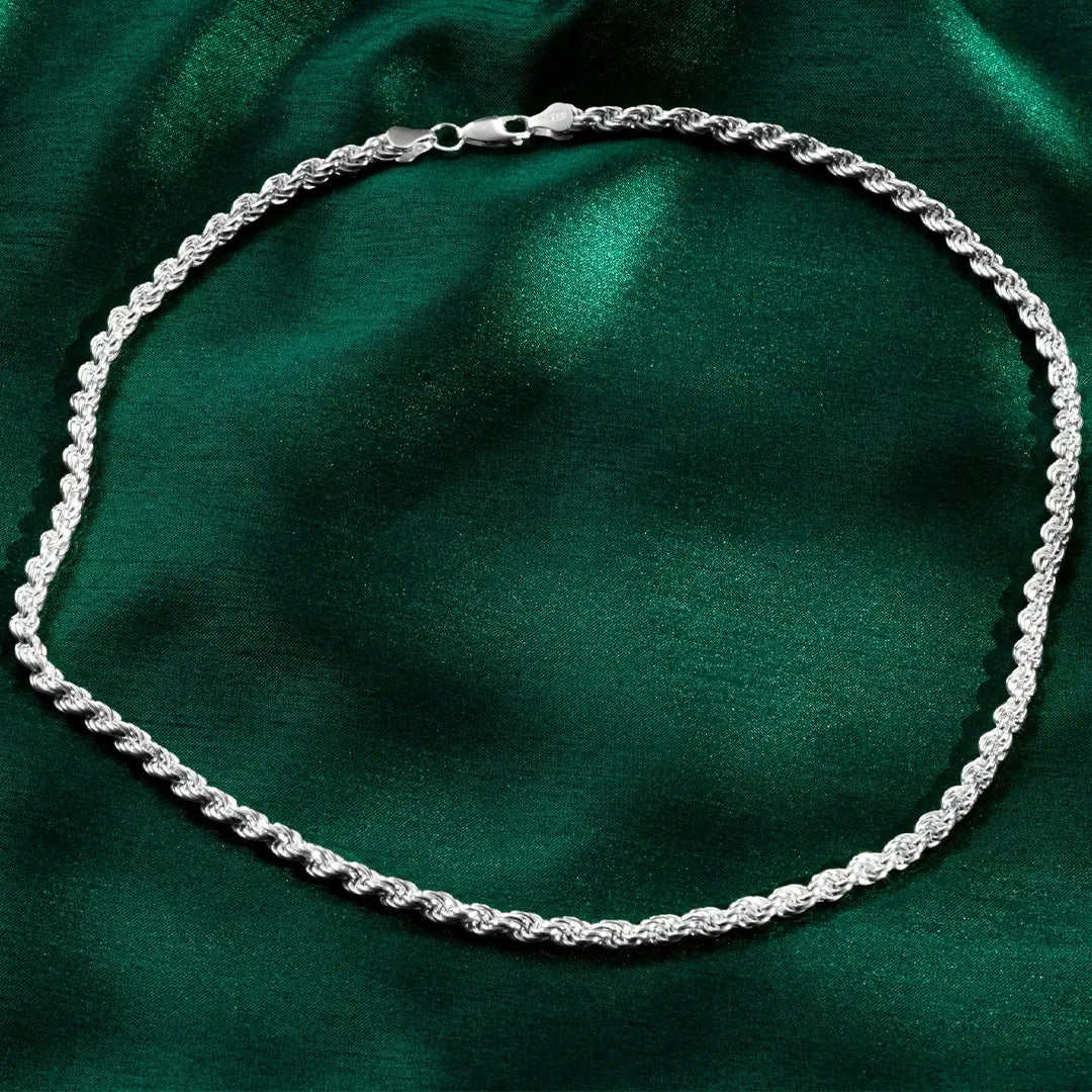 Silver rope-style necklace arranged in an oval shape on deep green satin fabric