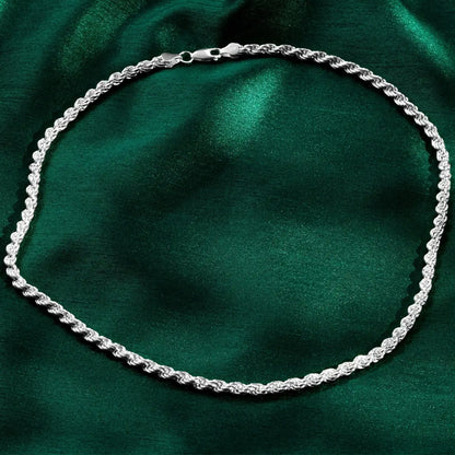 Silver rope-style necklace arranged in an oval shape on deep green satin fabric