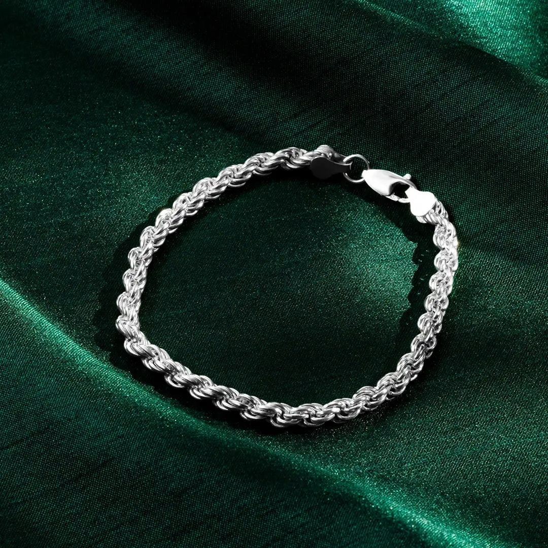 Close-up of a silver rope bracelet with a lobster clasp resting on green satin fabric