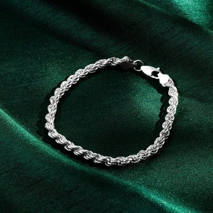 Close-up of a silver rope bracelet with a lobster clasp resting on green satin fabric