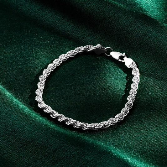 Close-up of a silver rope bracelet with a lobster clasp resting on green satin fabric