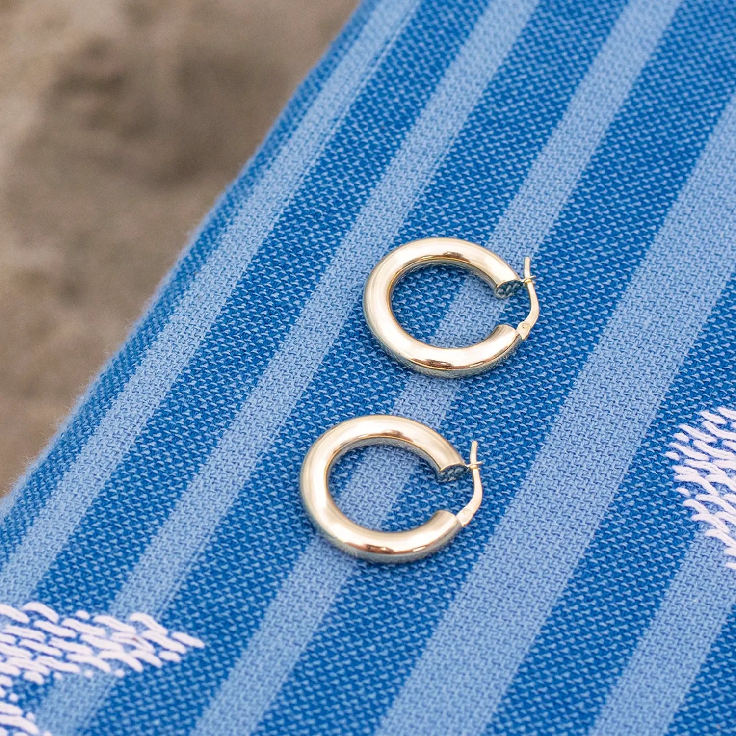 photograph of a large pair of gold hoop earrings on a beach towel