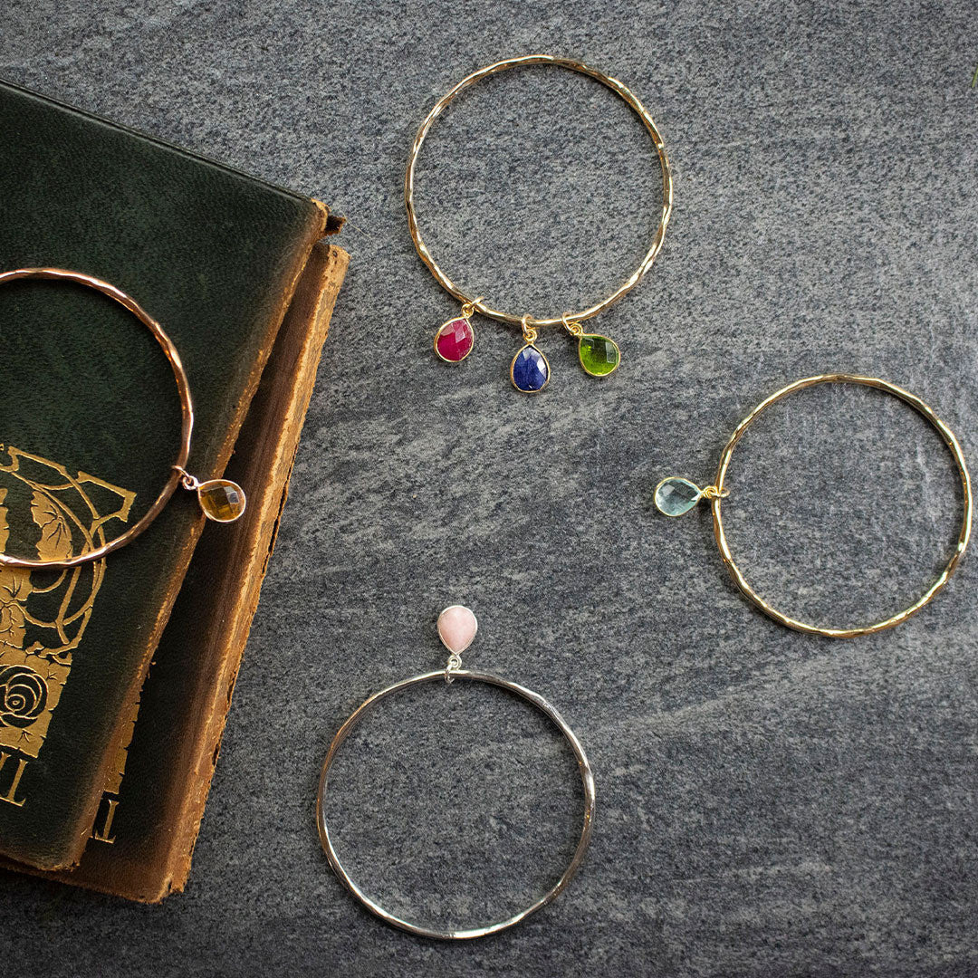 four charm bangles with different birth stones  and a book on a piece of fabric
