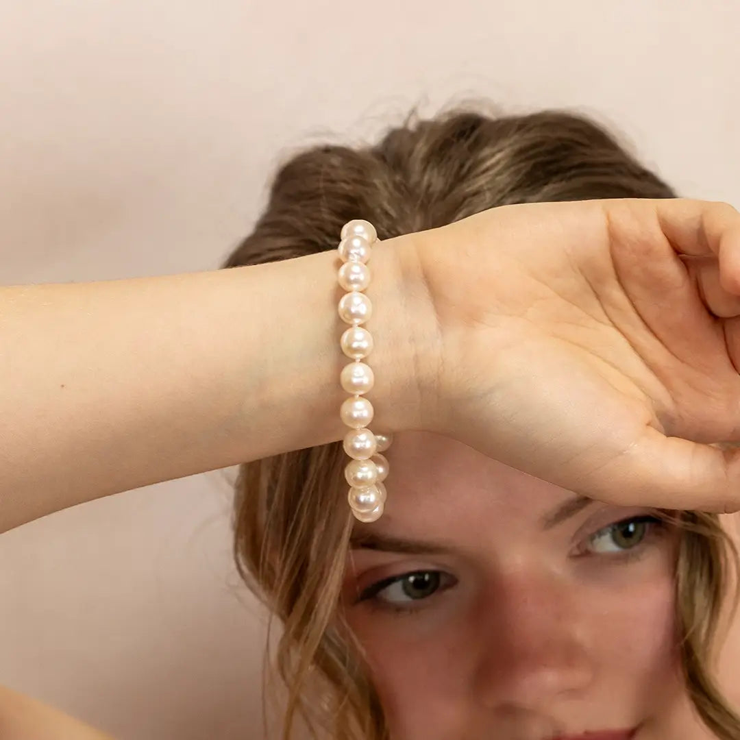Close-up of ivory freshwater pearl bracelet on a woman’s wrist, showing glossy round pearls strung together in a classic elastic design against a soft neutral background.