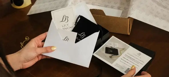Lily Blanche jewellery care kit with a black branded pouch, polishing cloth and care instructions beside an open jewellery box.
