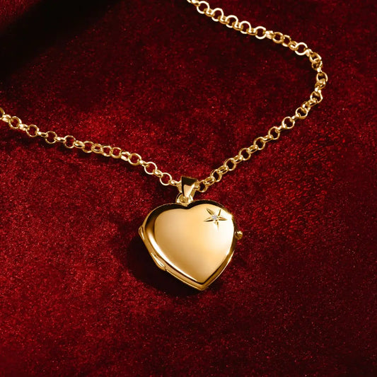 A gold heart-shaped locket with a small diamond on the front, displayed on a rich red velvet background. The locket hangs from a gold chain, catching the light with a polished shine.