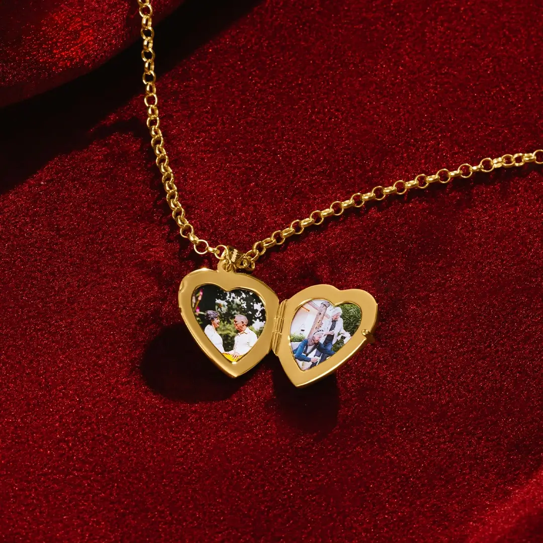 An open gold heart-shaped locket resting on red velvet, showing two small photos inside—each framed by the heart-shaped interior. The gold chain lies gracefully around the locket.