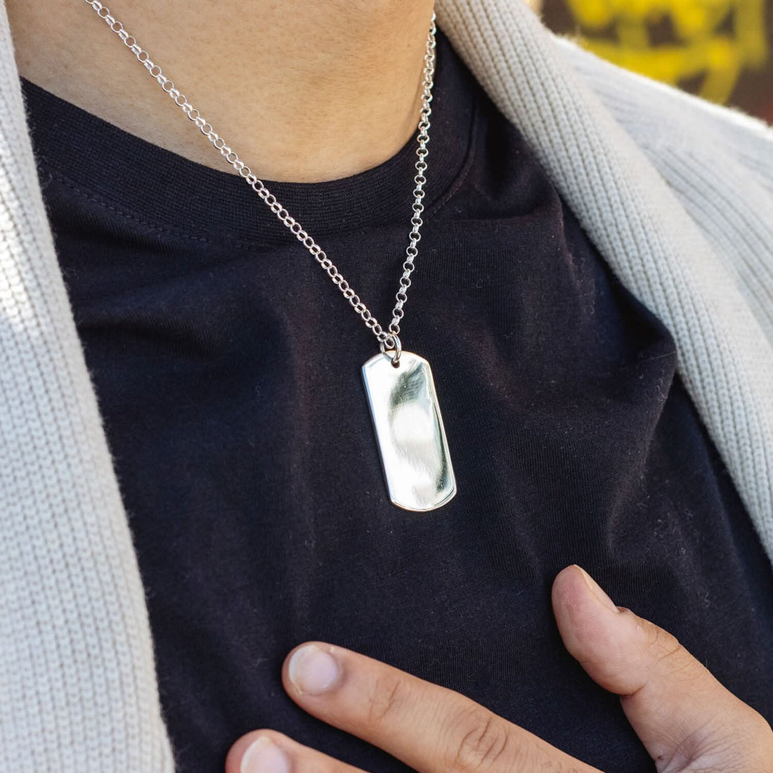 Solid silver extra-large dog tag worn by a male modelw wearing a black top and white knitted jacket.
