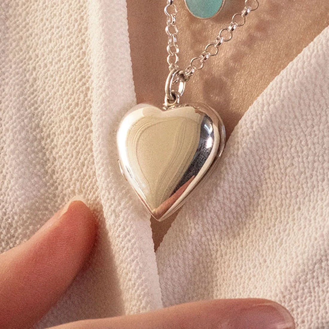 close up image of large 2 photo heart locket in silver being worn by woman 