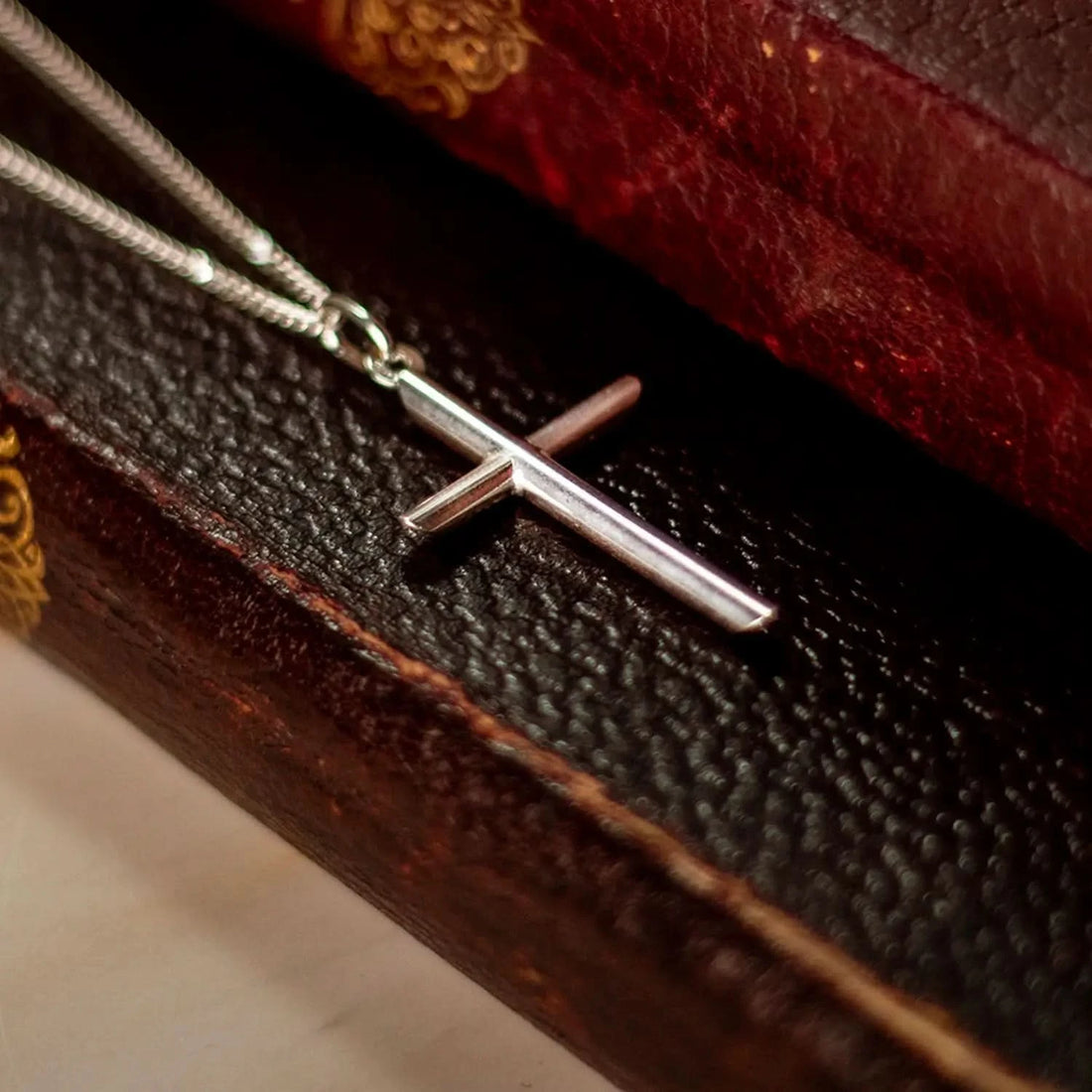 silver cross necklace, sturdy silver curb chain, high polish finish, rounded edges, unisex pendant for men and women, sitting on leather books.
