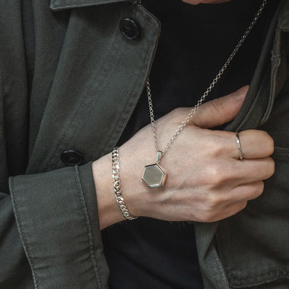 Close-up of man wearing a sterling silver Cuban link bracelet, hexagon pendant necklace, and silver ring with a dark jacket.