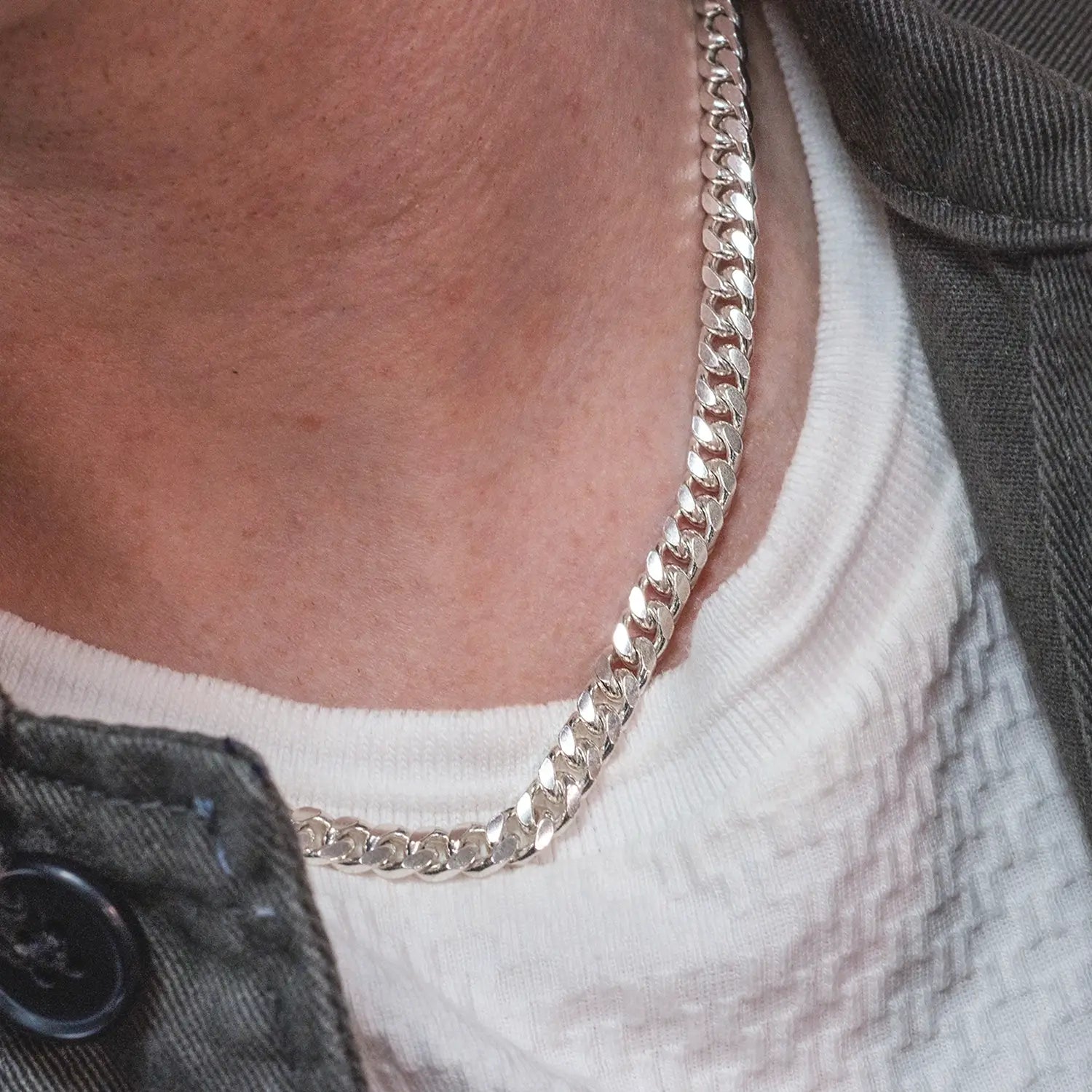 Close-up of a sterling silver Cuban link chain necklace worn with a white textured shirt and dark jacket