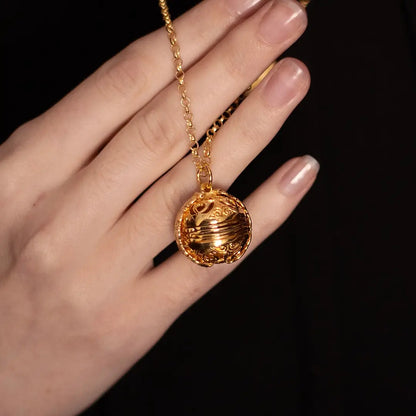 Lily Blanche gold Memory Keeper locket held against a hand, showing its ornate spherical design and chain.