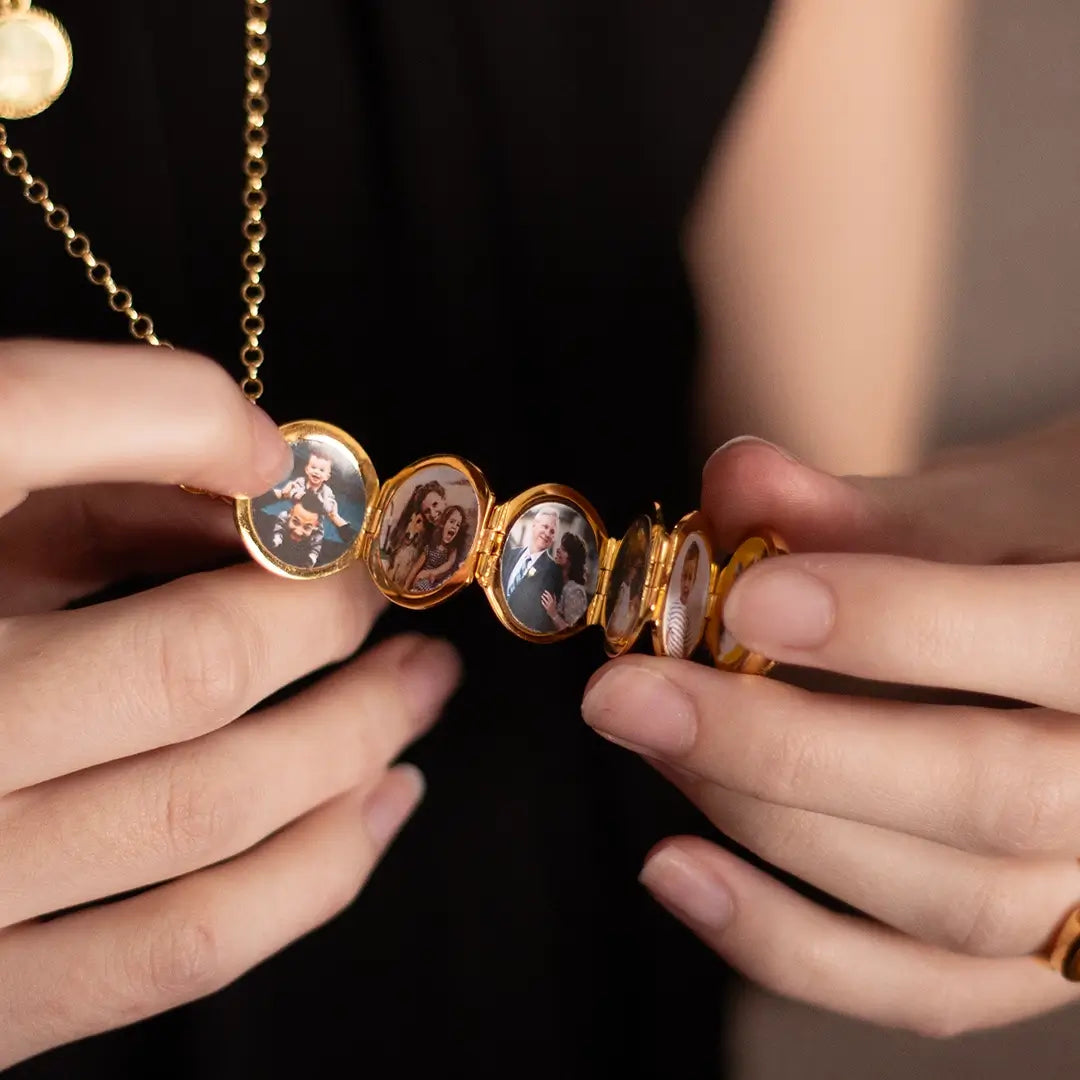 Hands holding a Lily Blanche gold Memory Keeper locket unfolded to reveal six family photographs.