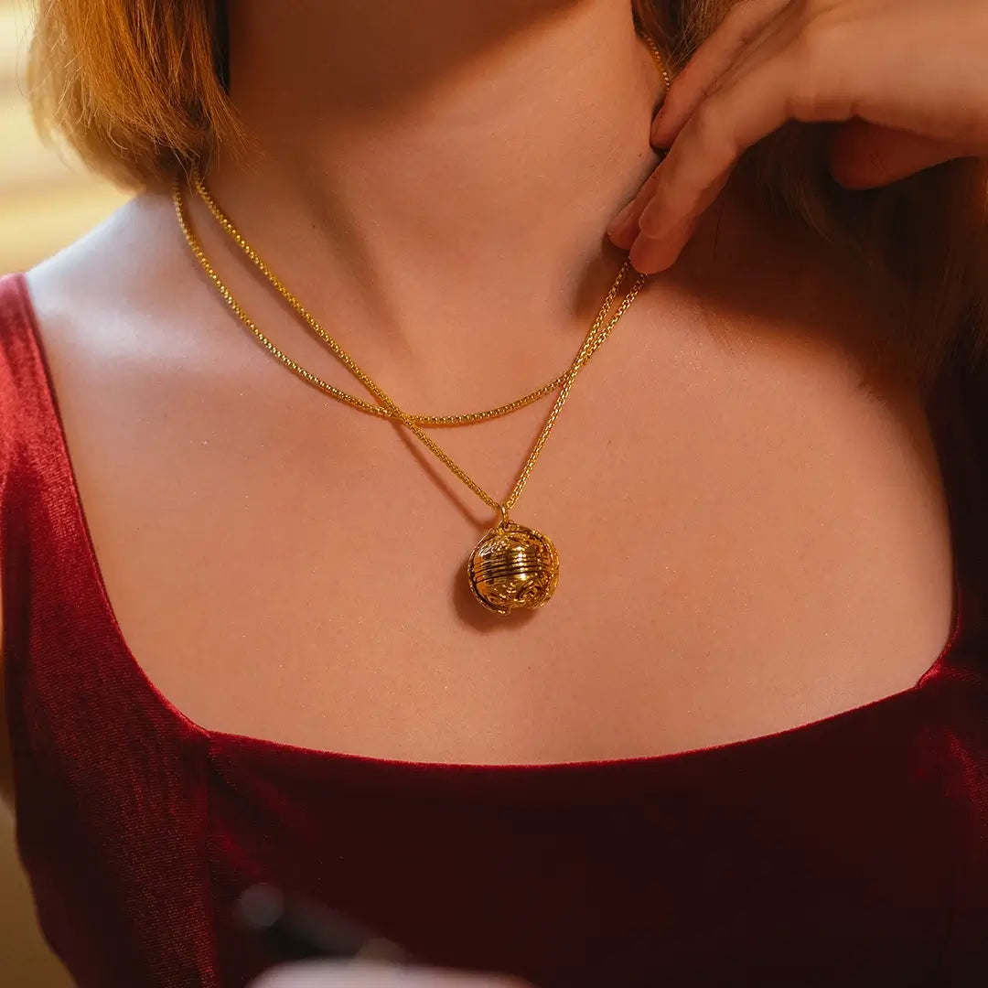 Woman wearing a Lily Blanche gold Memory Keeper locket layered with a shorter gold chain above a burgundy top.