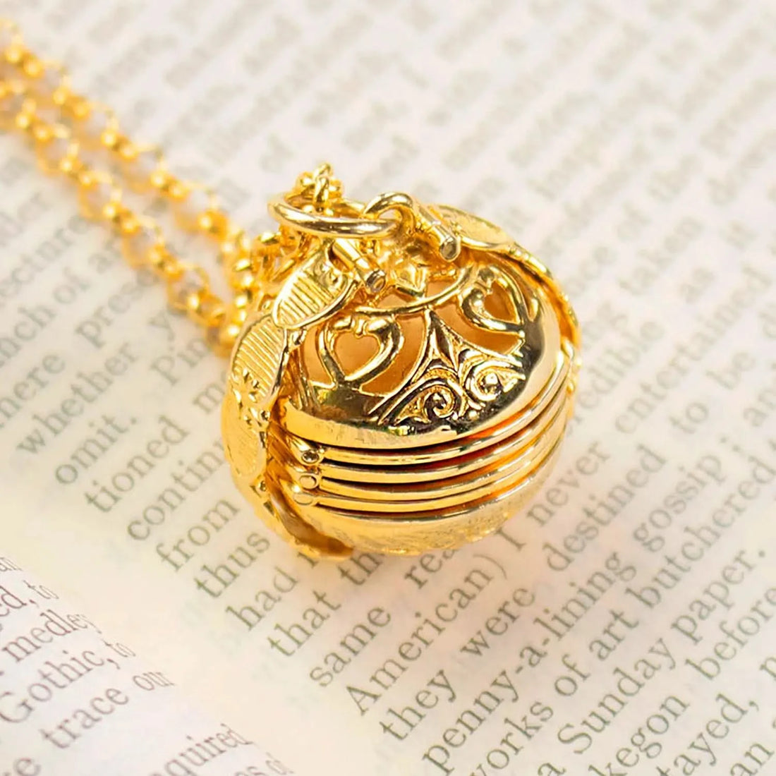 18 carat gold six photo Memory Keeper Locket® closed with a gold vermeil belcher chain photographed on an open book