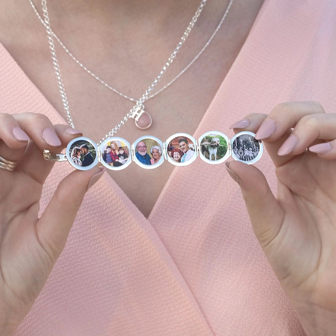 Model's hands holding an open sterling silver Memory Keeper Locket filled with six photos. Model is wearing a pink top and also wearing a layered pink opal birthstone pendant 