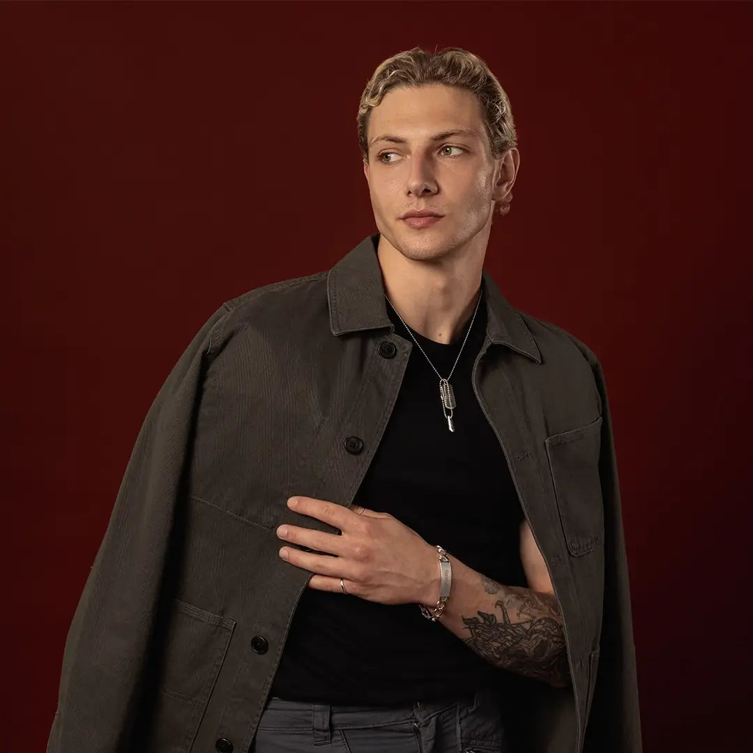 Male model wearing a sterling silver double dog tag necklace and engraved ID bracelet against a dark red background