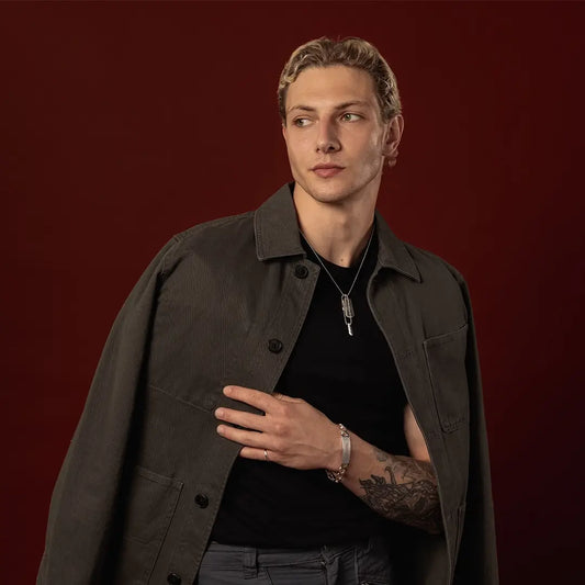 Male model wearing a sterling silver double dog tag necklace and engraved ID bracelet against a dark red background