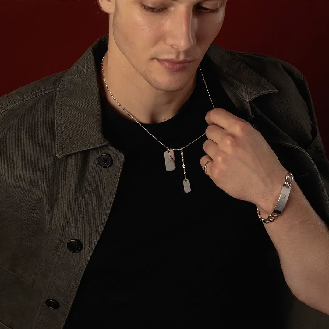 Male model holding a sterling silver double dog tag necklace, showing the personalised tags and engraved ID bracelet