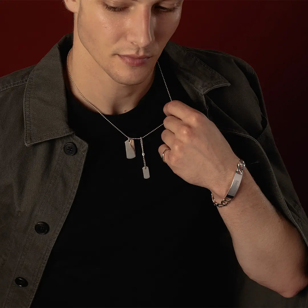 Close-up of male model wearing a sterling silver double dog tag necklace and engraved silver ID bracelet