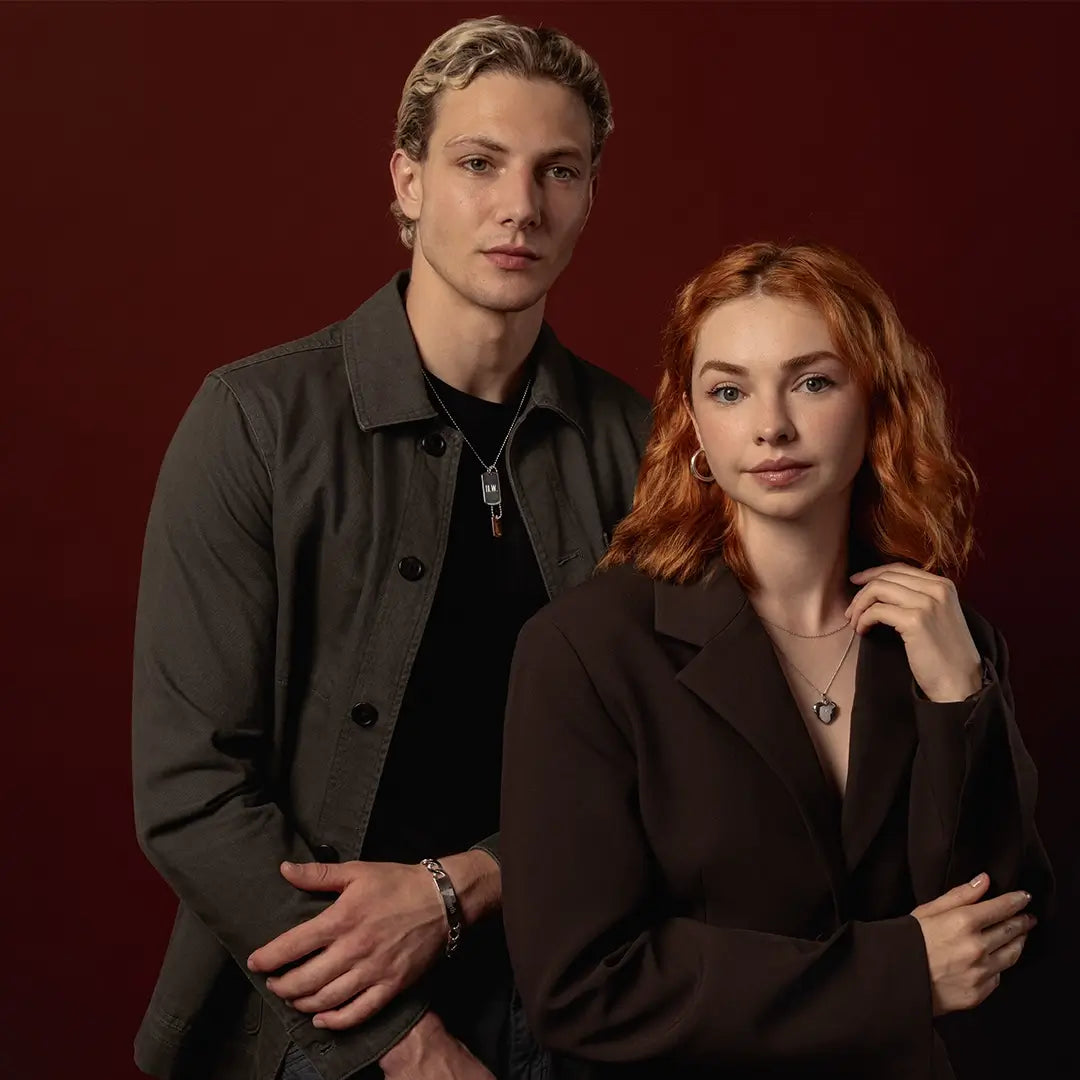 Male model wearing an engraved silver ID bracelet and dog tag alongside female model wearing a white gold diamond heart locket