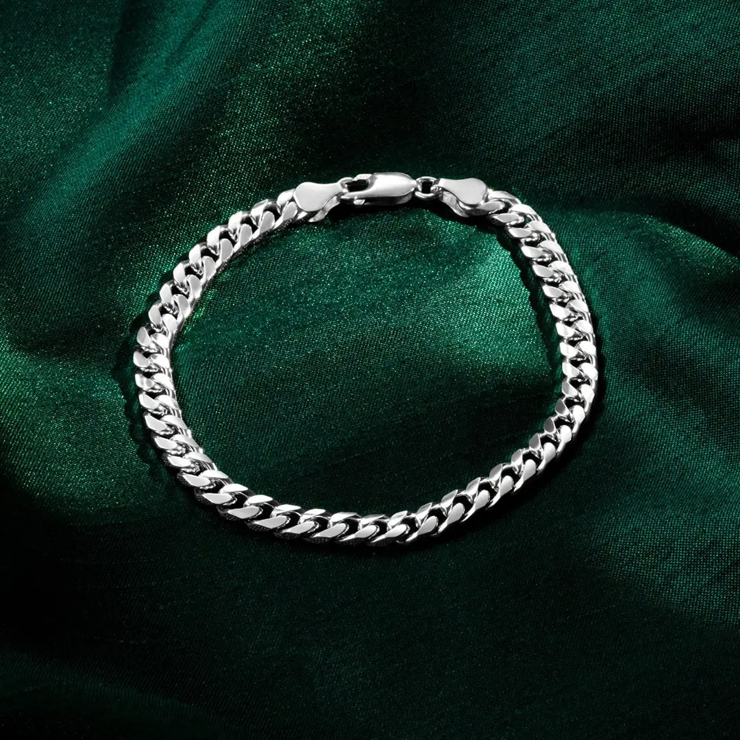A polished silver Cuban-link bracelet with a lobster clasp displayed in a circular shape on dark green satin fabric.