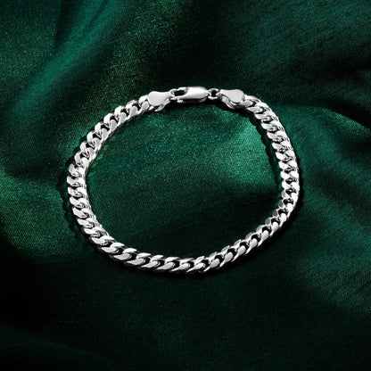 A polished silver Cuban-link bracelet with a lobster clasp displayed in a circular shape on dark green satin fabric.