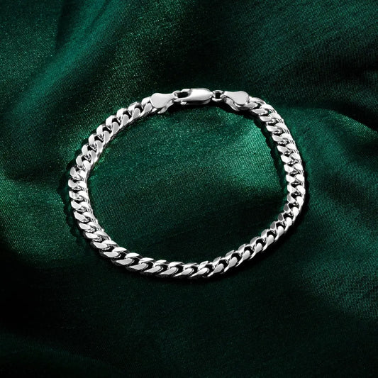 A polished silver Cuban-link bracelet with a lobster clasp displayed in a circular shape on dark green satin fabric.