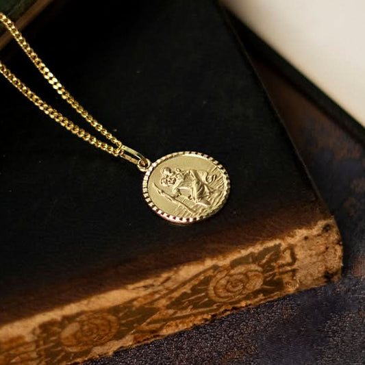 Close-up of men’s solid 9ct gold St Christopher pendant on a gold chain over a black book.
