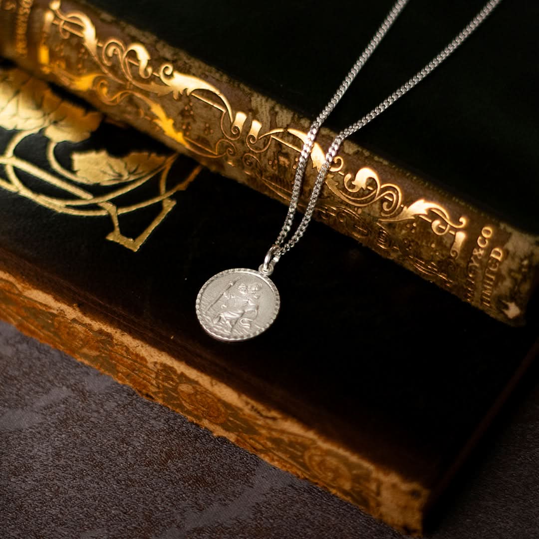 photograph of a silver round Saint Christopher necklace with chain placed on two books
