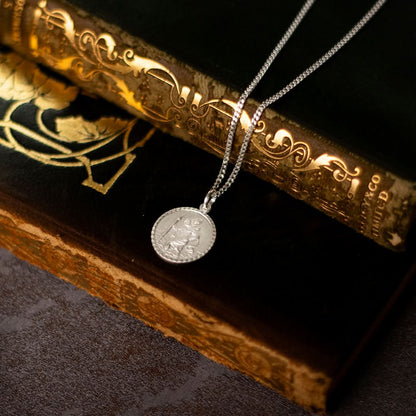 silver Saint Christopher necklace with chain placed on two books