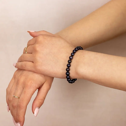 Close-up of midnight black freshwater pearl bracelet worn on a woman’s wrist, featuring glossy round dark pearls strung in a classic elastic design against a soft neutral background.