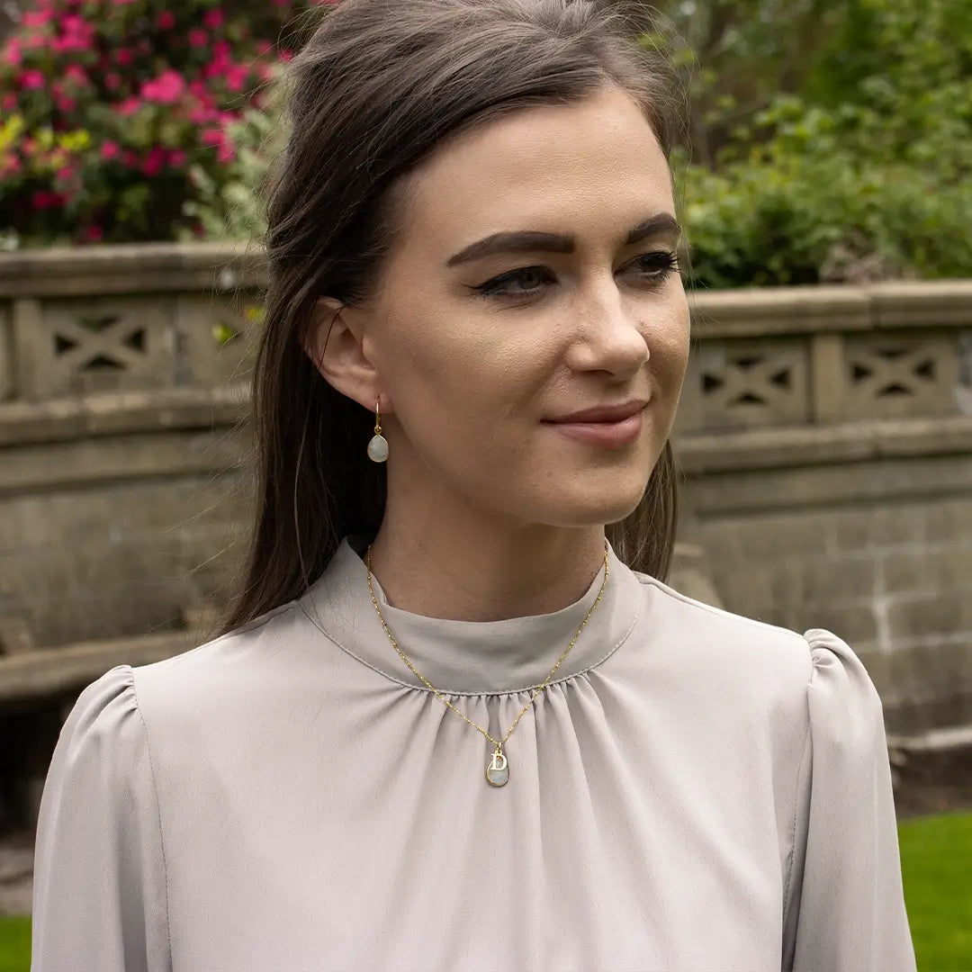 Gold moonstone initial necklace and matching moonstone drop earrings worn by a model, featuring faceted moonstone gemstones set in gold vermeil.