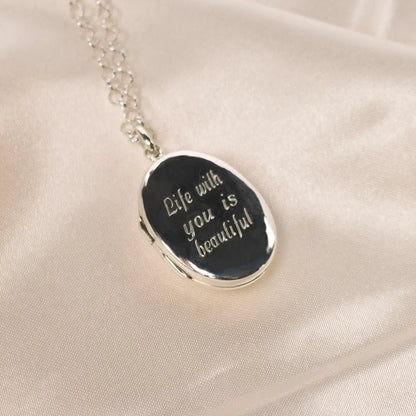 Sterling silver oval locket necklace engraved with the words “Life with you is beautiful”, displayed on soft cream fabric.
