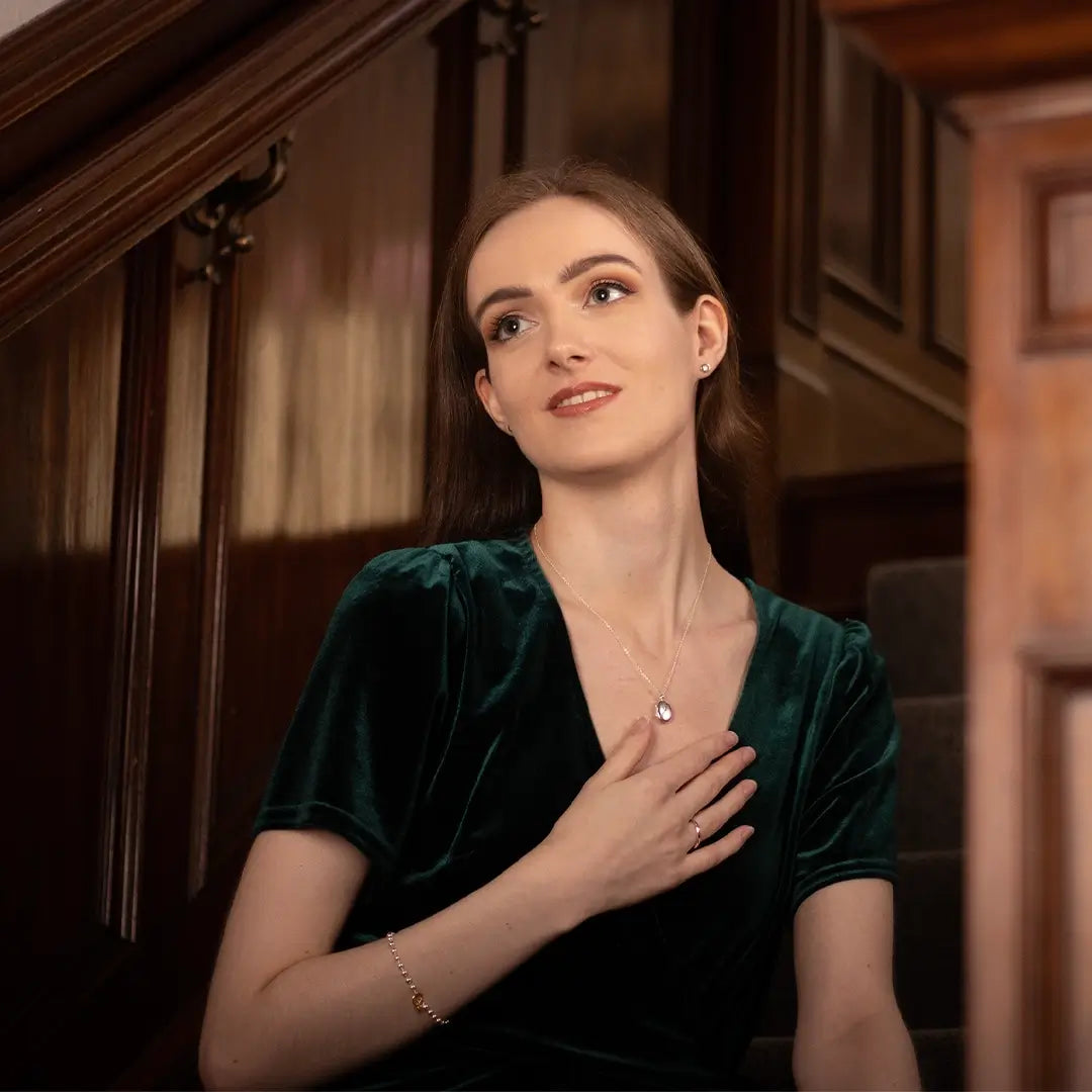 Woman wearing a sterling silver oval diamond locket necklace, styled with a deep green velvet dress in a classic interior setting.
