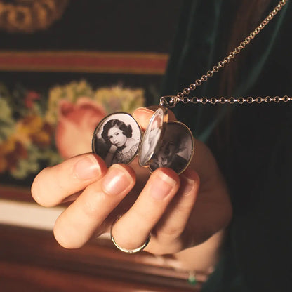 Close-up of an open sterling silver expanding oval photo locket showing black-and-white portrait photographs inside, held delicately in hand.
