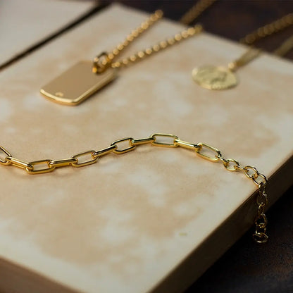 Gold paperclip chain necklace with extender links, photographed on a neutral stone surface alongside gold pendants