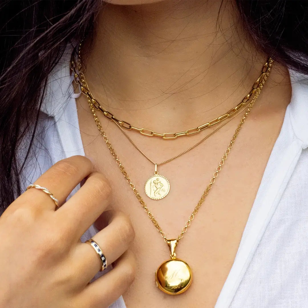 Gold paperclip chain necklace styled layered with a round gold locket and coin pendant, worn on the neck