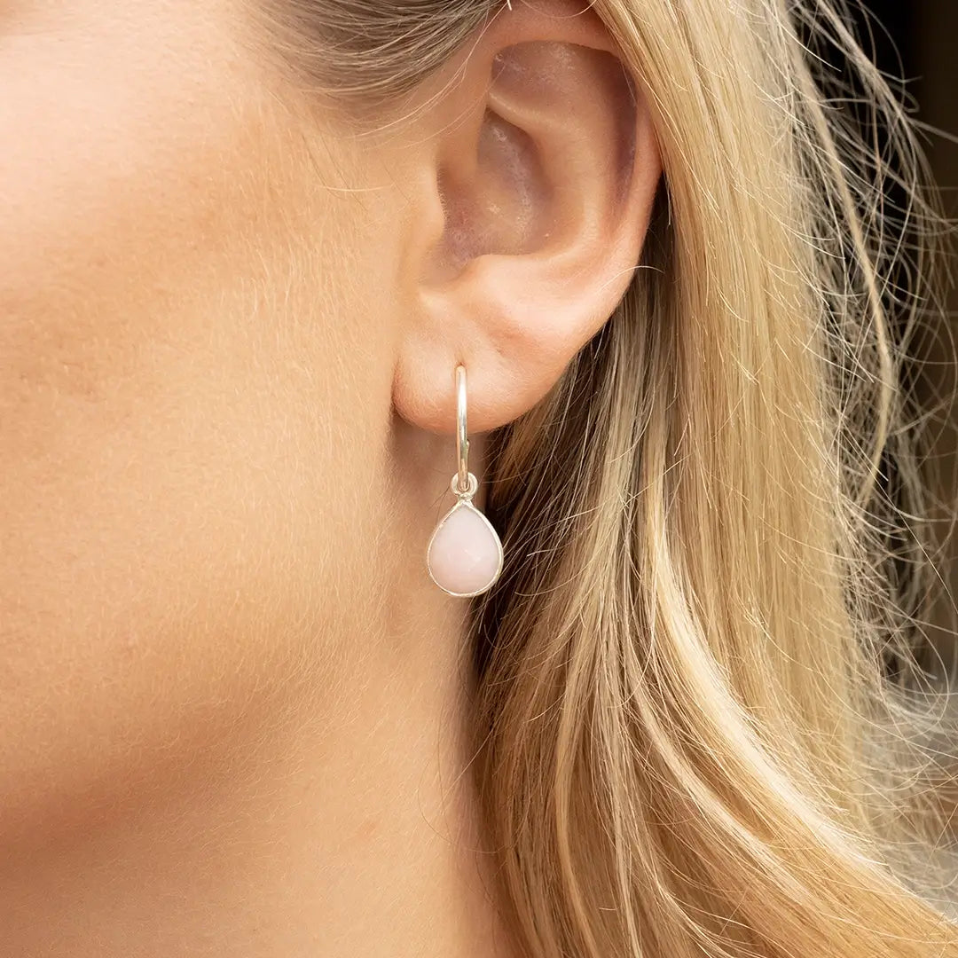 Sterling silver pink opal drop hoop earring worn on the ear, featuring a soft blush pink opal gemstone in a teardrop setting.