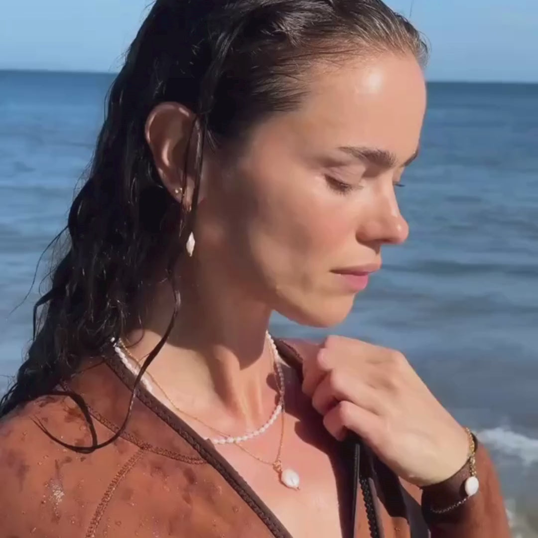 Video of a brown haired model wearing the Lily Blanche coin pearl set, necklace, bracelt and earrings, with a Fulmar wetsuit, emerging from the sea